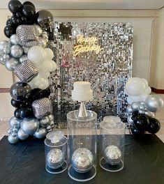 a table topped with lots of silver and black balloons next to a cake on top of a plate