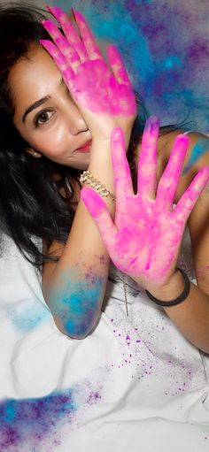 a woman laying on top of a bed covered in pink and blue powder holding her hands up