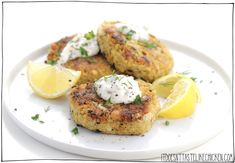 three crab cakes on a white plate with lemon wedges and sour cream drizzled on top