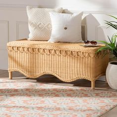 a wicker bench with pillows on it in front of a potted plant and rug