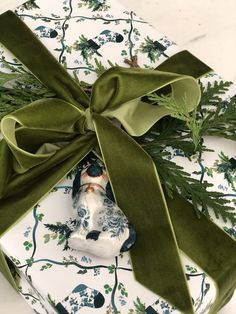 a present wrapped in green ribbon on top of a white plate with an ornament