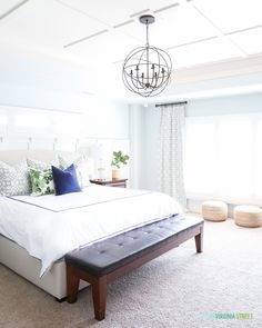 a bed with white sheets and pillows in a bedroom next to a chandelier