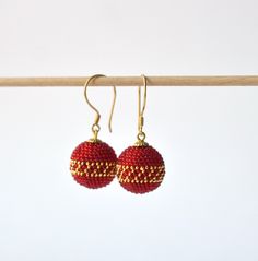 pair of red and gold beaded earrings hanging from a clothes line against a white background