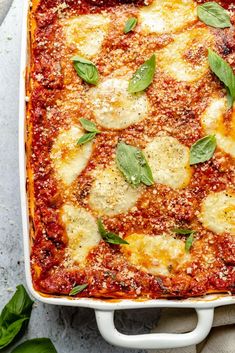 a casserole dish with cheese and spinach on top, garnished with fresh basil