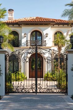 an iron gate is in front of a white stucco house with palm trees and potted plants