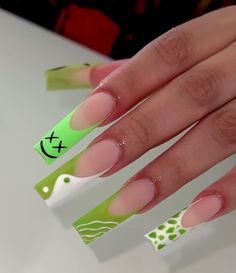 a woman's hand with green and white nail polish on it, holding onto the tip of her nails