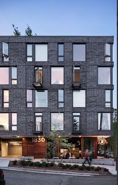 an apartment building with lots of windows and people walking on the sidewalk