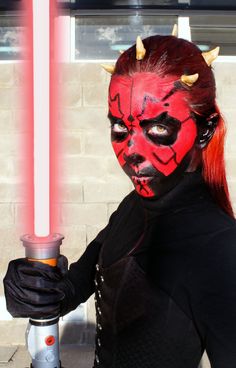 a woman dressed as darth vader with red hair and horns holding a light saber