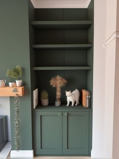 a white cat sitting on top of a green book shelf next to a potted plant