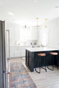 a kitchen with two stools in front of the island and an area rug on the floor