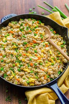 a skillet filled with rice and vegetables on top of a wooden table next to green beans