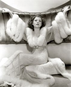 an old photo of a woman sitting on a couch with fur stoles around her neck