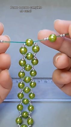 two hands are holding green beads and threading them together to make a beaded necklace