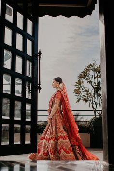 a woman in a red and gold bridal gown is walking towards an open doorway