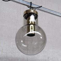 a clear glass light bulb hanging from a ceiling fixture with a metal bar in the background