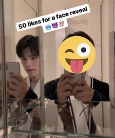 a man taking a selfie in front of a mirror with an emoticive sticker on his face