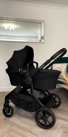 a black stroller sitting on top of a hard wood floor next to a mirror