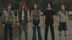 five people standing in the middle of a road with blood all over their shirts and pants