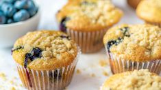 several blueberry muffins are sitting on a white surface next to a bowl of berries