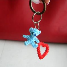 a person holding a keychain with a teddy bear beaded on it's side