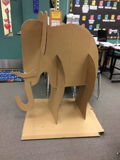 an elephant made out of cardboard sitting on top of a wooden table in a classroom