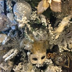 a white christmas tree with silver and gold ornaments on it's branches, including a mask