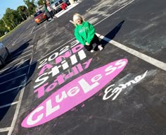 a woman standing in the middle of a parking lot next to a pink and white sign