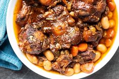 a bowl filled with meat and beans on top of a blue cloth next to a spoon