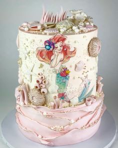 a three tiered cake decorated with mermaids and seashells