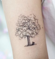 a small tree tattoo on the left inner arm, with a cat sitting under it