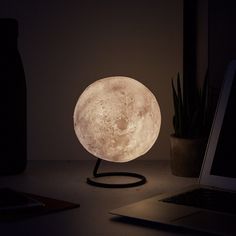 the moon lamp is sitting on top of a desk next to a laptop and plant