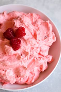 a bowl filled with whipped cream and raspberries on top of a white table