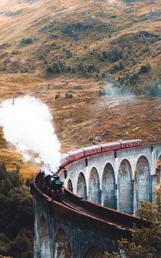 a train traveling over a bridge with steam coming out of it's chimneys