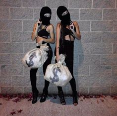 two women wearing masks and holding bags in front of a brick wall