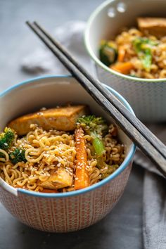 two bowls filled with noodles and vegetables next to chopsticks