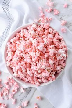 a bowl filled with pink popcorn on top of a white table cloth next to other items