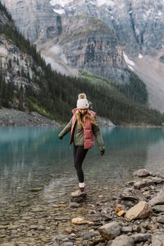 a woman is walking along the shore of a mountain lake