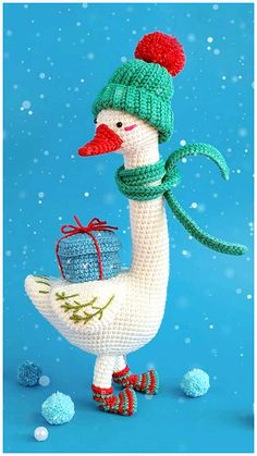 a knitted white bird with a green hat and scarf holding a blue gift box