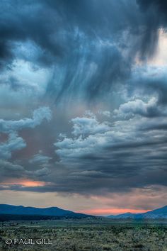 the sky is filled with dark clouds and some mountains in the distance are seen behind it