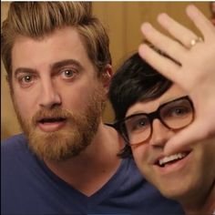 two men with glasses and beards posing for the camera, one holding his hand up