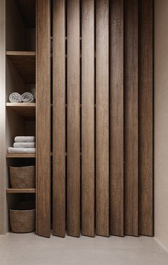 a closet with wooden doors and shelves filled with folded towels, baskets and blankets on the floor