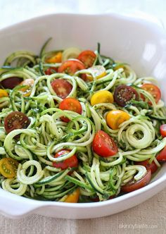 a white bowl filled with zucchini noodles and tomatoes on top of a table