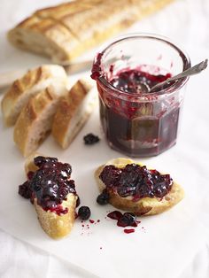 some bread and jam on a white plate next to a glass of jelly with a spoon in it