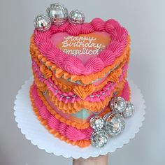 a birthday cake with pink and orange frosting on top is being held up by someone's hand