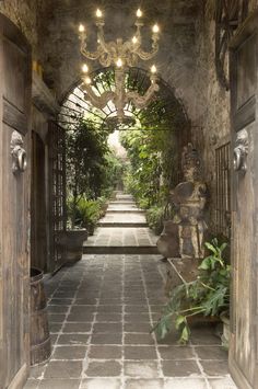 an archway leading into a lush green garden with chandeliers hanging from the ceiling