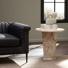 a table with books on it in front of a chair and window next to a couch