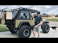 a man standing next to a green and tan jeep with a dog on the side