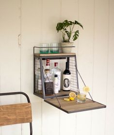 a shelf with bottles and glasses on it next to a chair in front of a wall