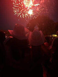 two people wearing hats watching fireworks in the sky