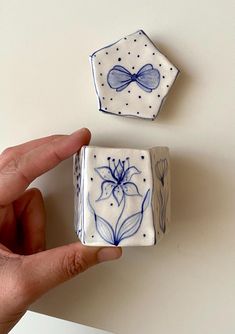 a hand is holding two small blue and white tiles with flowers on them, one has a bow at the top